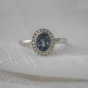 oval sapphire bezel set, with a halo of (20) bead-set diamonds in a polished 14K white gold band.